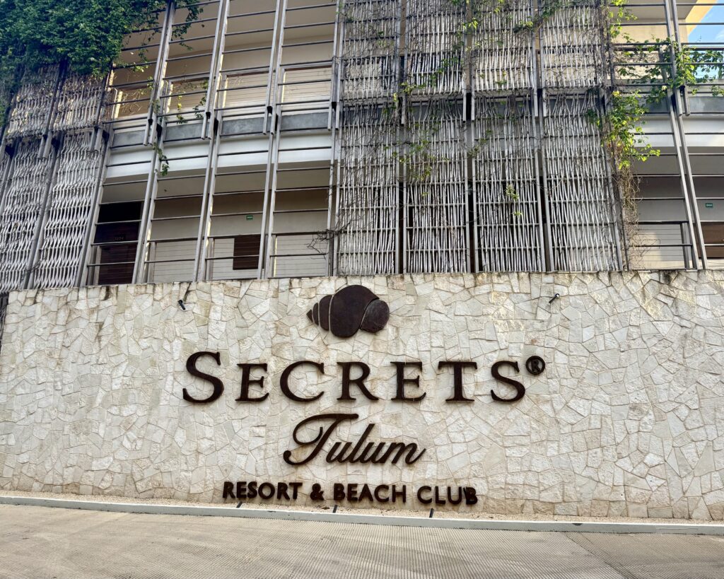 Entrance of Secrets Tulum Resort & Beach Club displayed on a stone wall, marking the main arrival area of the luxury adults-only resort in Tulum, Mexico