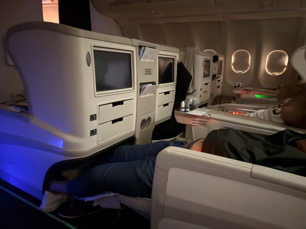 Fiji Airways A330 business class angled-flat seat fully reclined in bed mode showing limited storage compartments and footwell space.